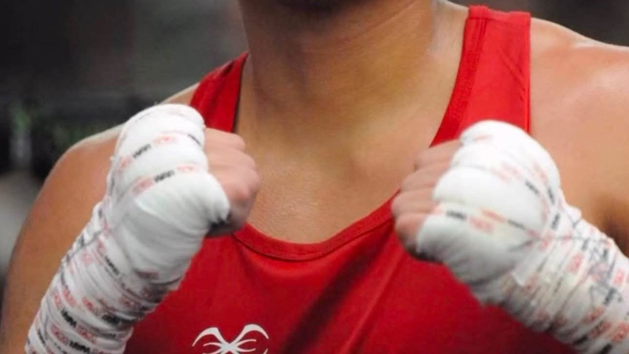 Close up of an Ironhand fighter in a red competition singlet, fists up in guard, both hands wrapped in gauze and tape