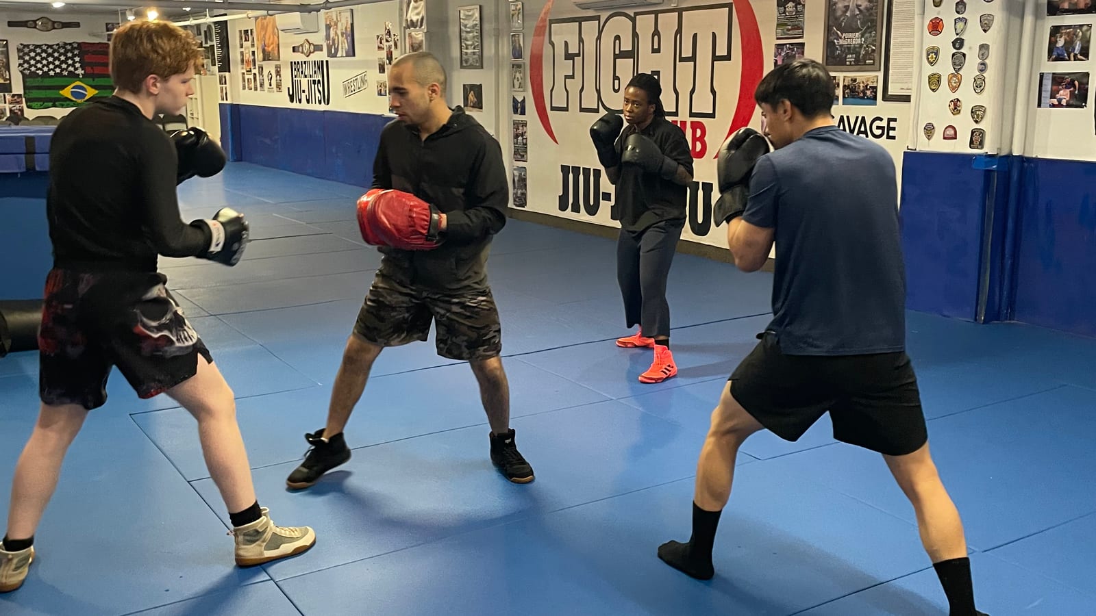 Four Ironhand boxers working partner drills in gloves while a coach holds the red mitts
